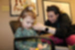 A doctor wearing a black jacket is examining the ears of a young child during a audiology exam.