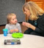 A speech language professional wearing a black jacket is using sign language to communicate with a y